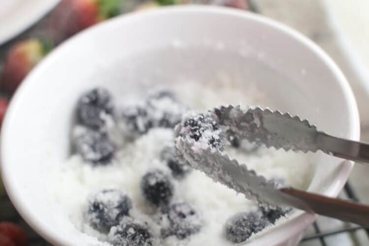 Using tongs to retrieve the blueberries from the bowl of sugar