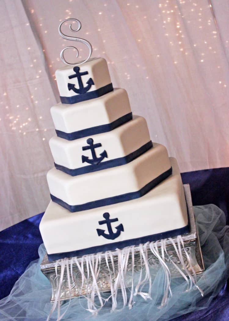White Hexagon Wedding Cake with Navy Anchors and ribbon borders displayed on a square silver cake stand.
