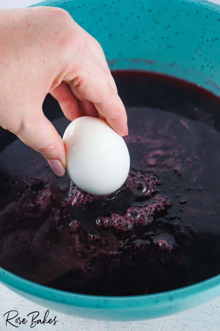 white egg being dipped into the black berry juice 