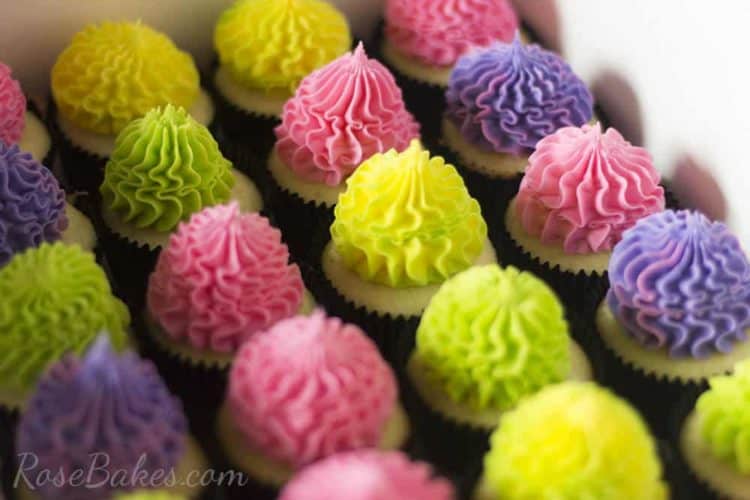 A picture of2 dozen pink, purple, green, and yellow cupcakes in a box