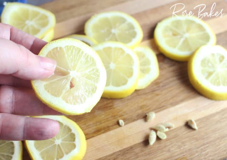 removing seeds from sliced lemons on a cutting board for candied lemons