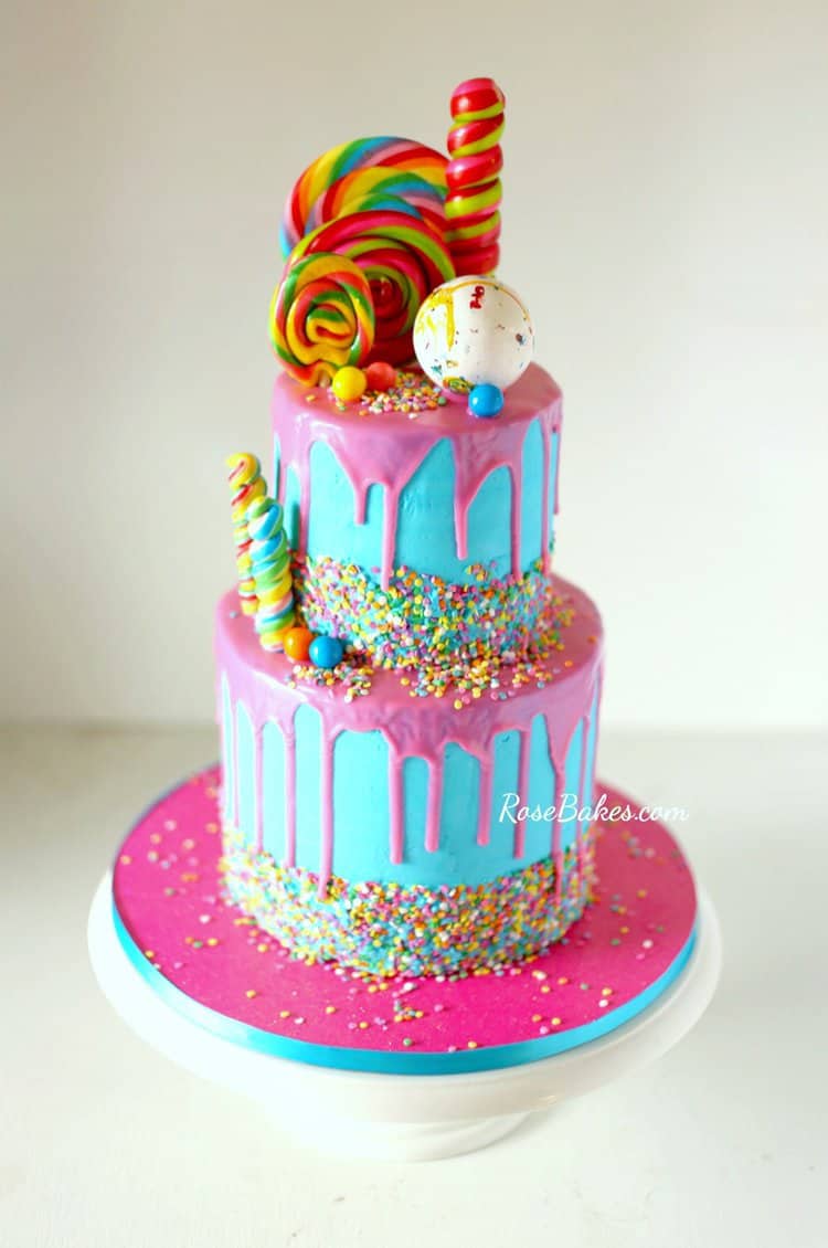 Super Easy Drip Cake Recipe (Canned Frosting Hack!) - a bright blue cake with bright pink canned frosting drip plus sprinkles and candies for decorations.