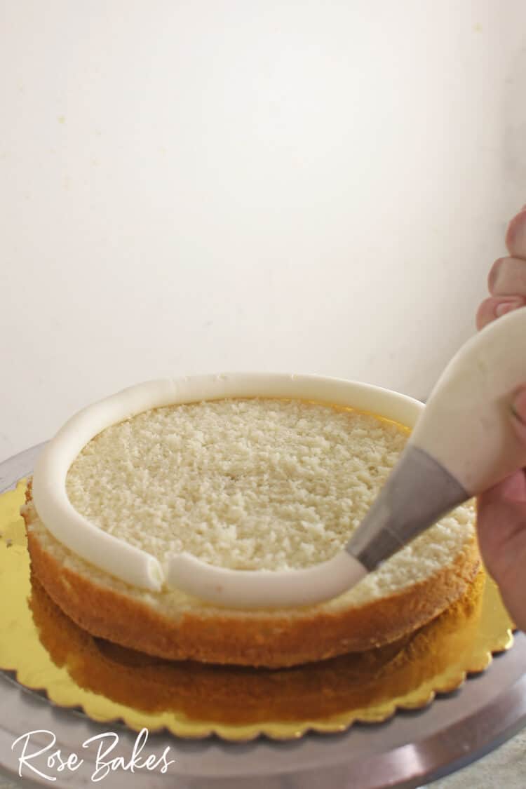 Buttercream dam being piped onto a layer of cake