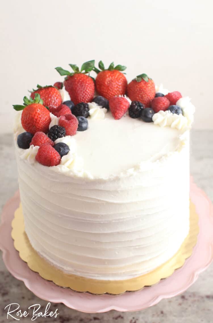Chantilly Cake with fresh berries  Displayed on a light pink scalloped cake stand.