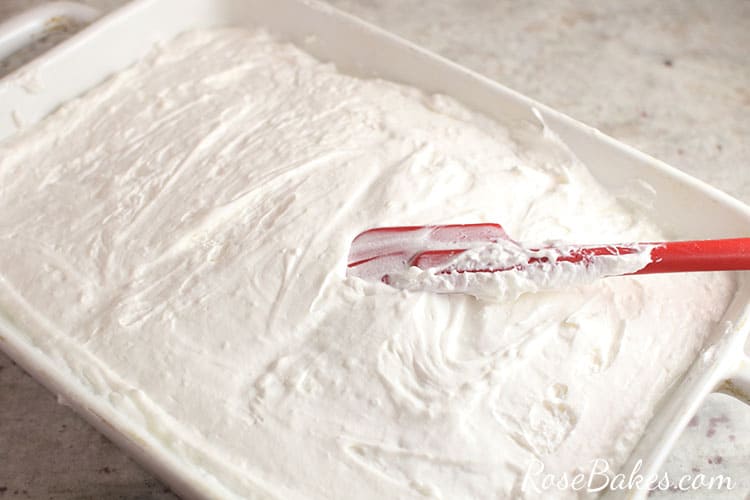 spreading cool whip mixture over the cake in the baking dish