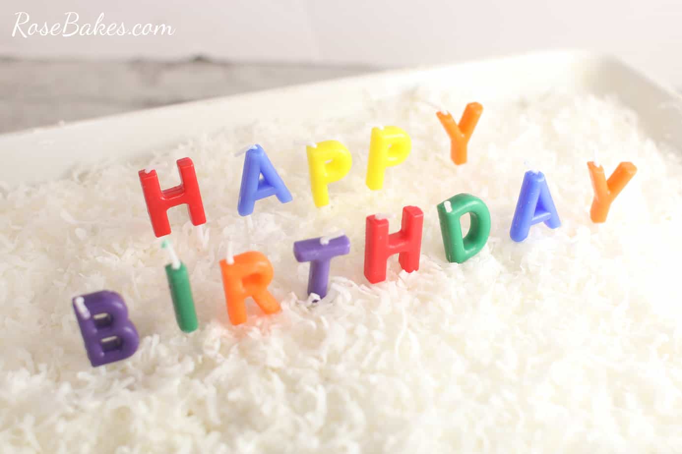 happy birthday candles in a coconut poke cake in a white baking dish