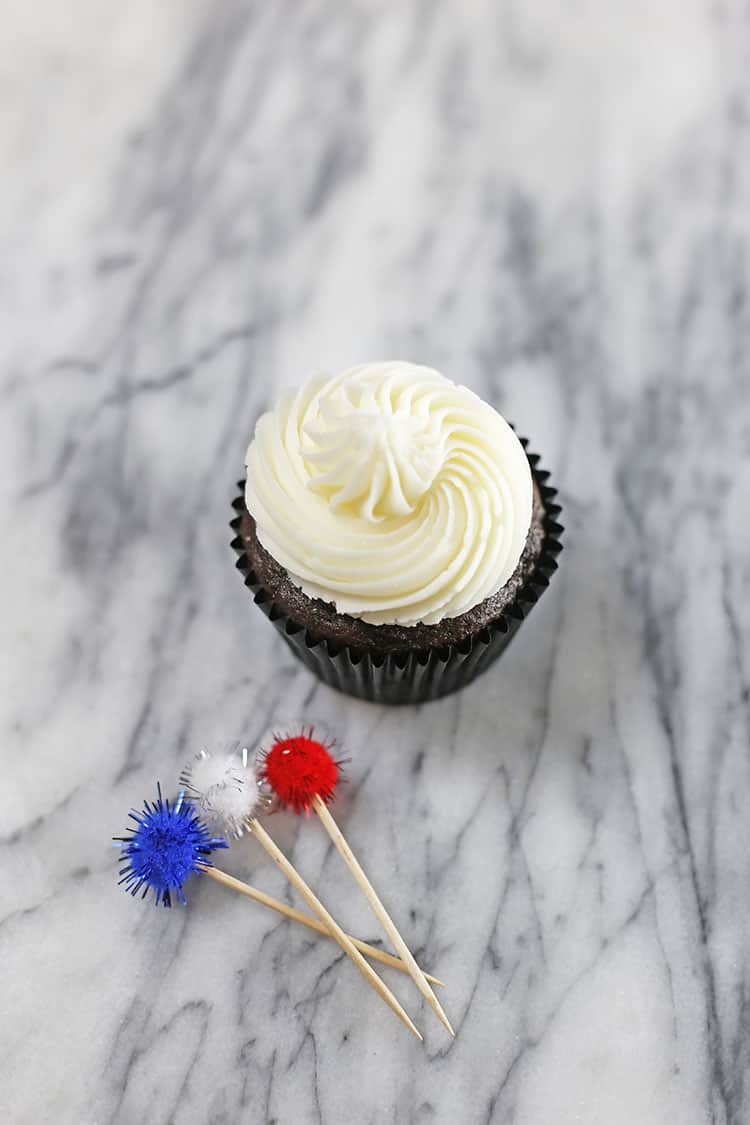 chocolate cupcake with vanilla frosting in a liner on a counter with pompoms on toothpicks