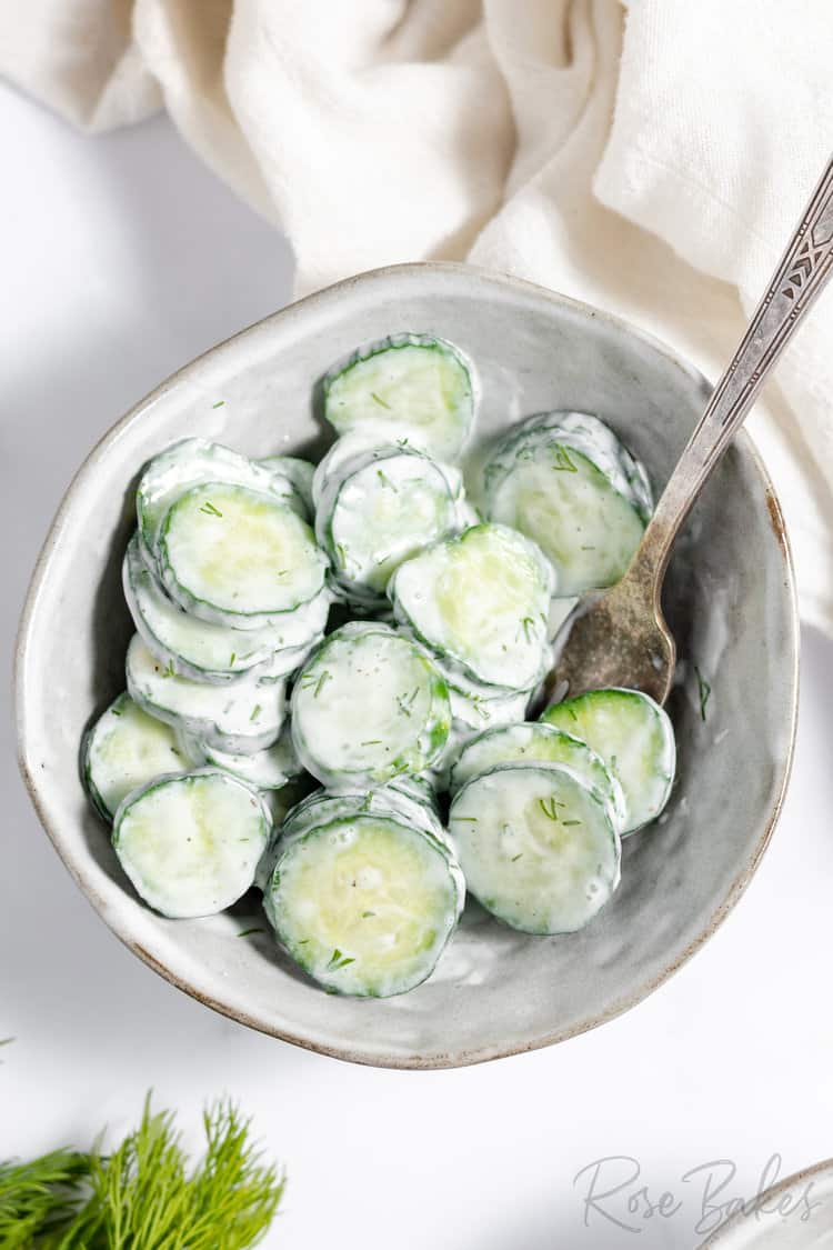 german cucumber salad tossed in a creamy white german dressing in a white bowl with a spoon