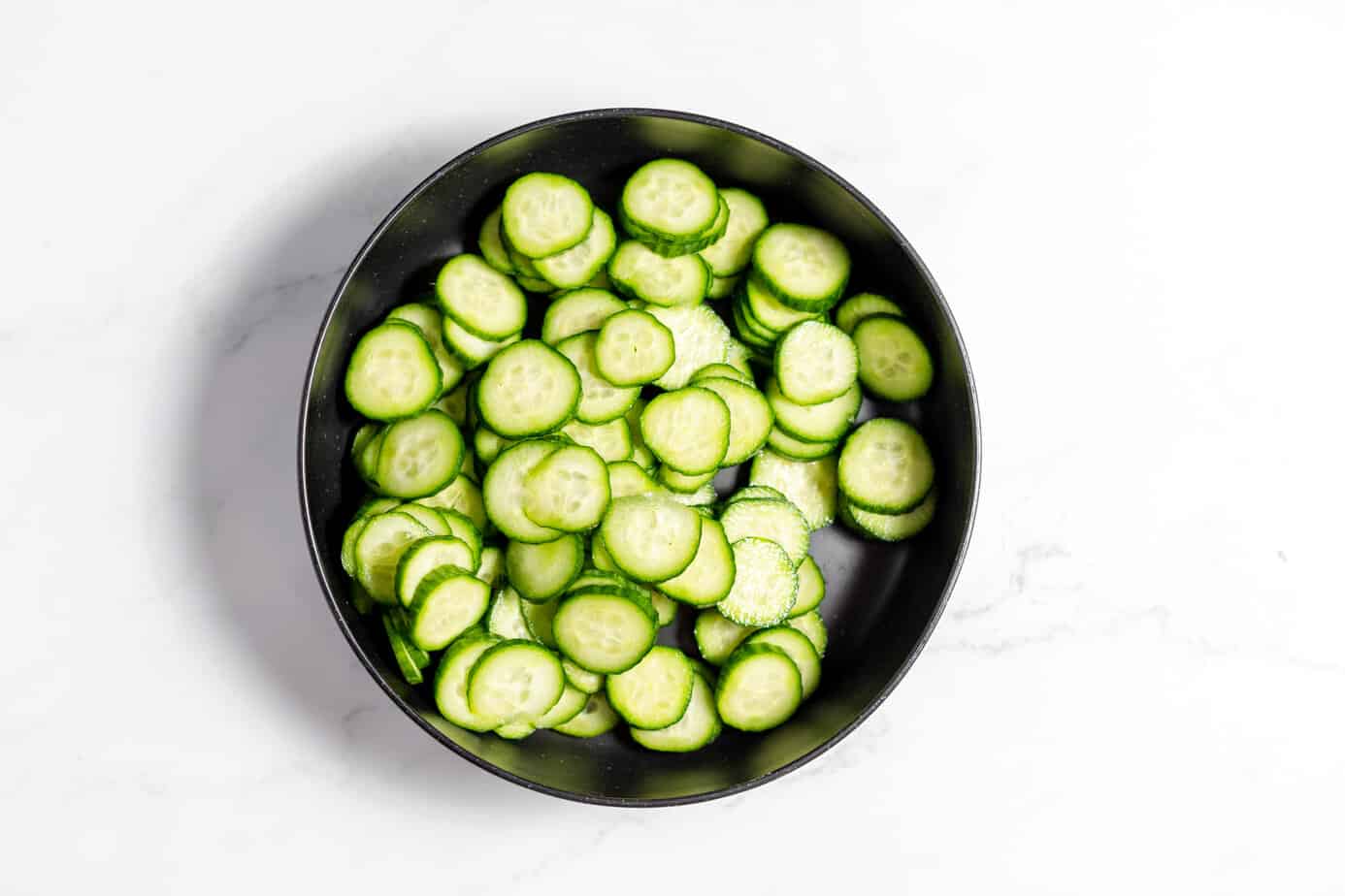 sliced cucumbers in a large black bowl