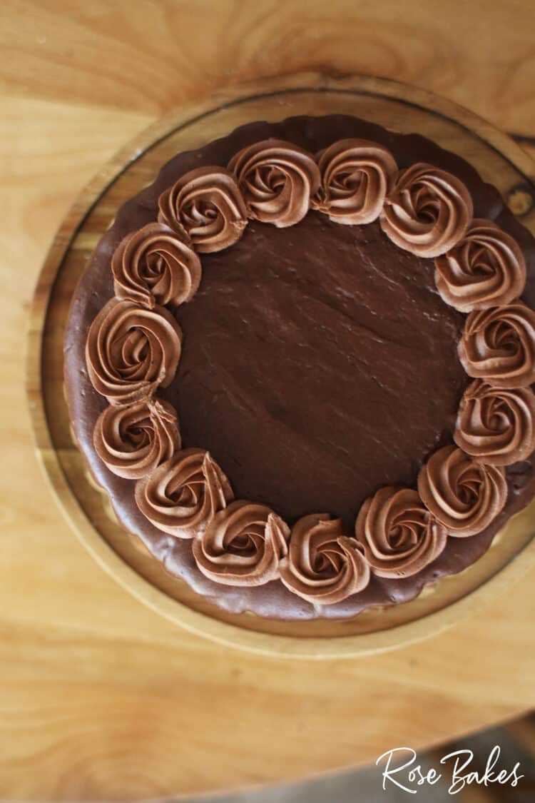 Top view of the chocolate cake with the dark brown chocolate drip and light brown chocolate rosettes contrasted on top.