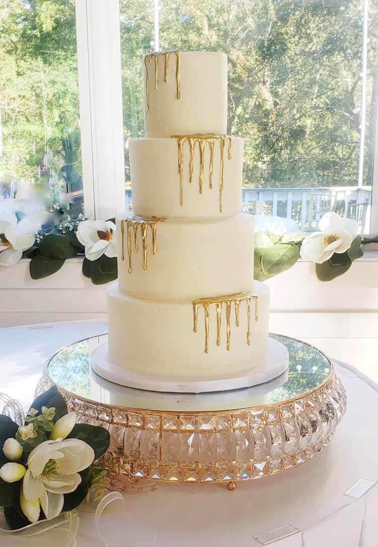 four tiered white wedding cake with gold drip on alternating edges