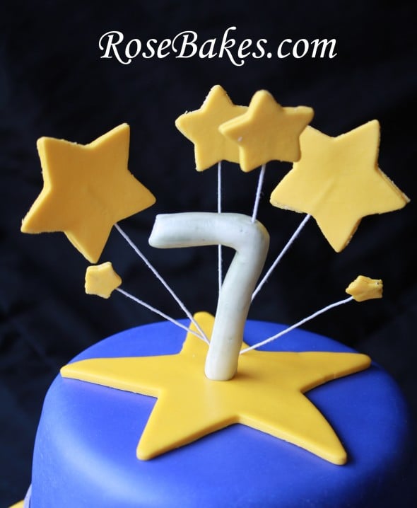 Stars on wires coming out of the top of the cake with a 7 topper.