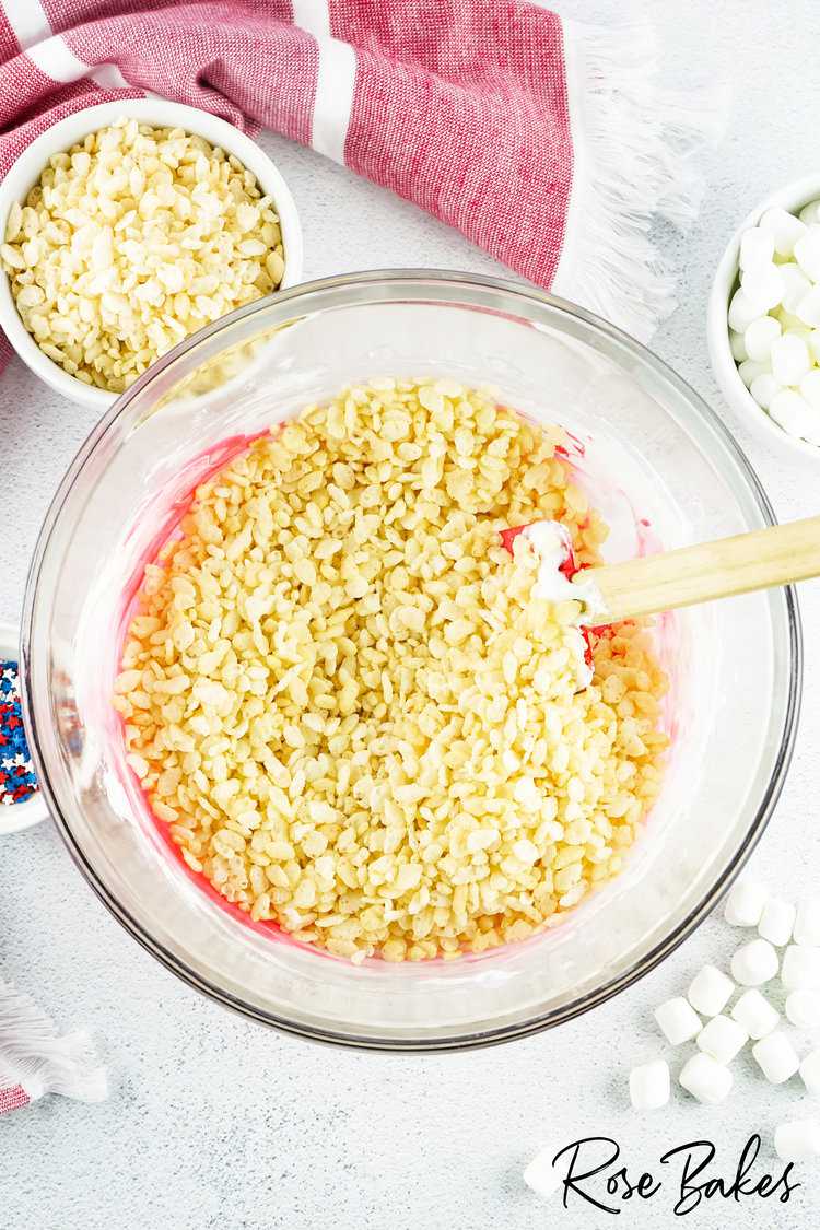 rice cereal added to melted butter and marshmallows in a clear bowl with red coloring 