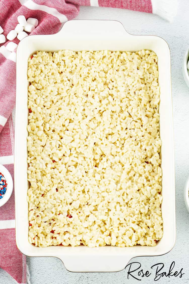 original rice krispies pressed flat in a white baking dish on top of red rice krispies