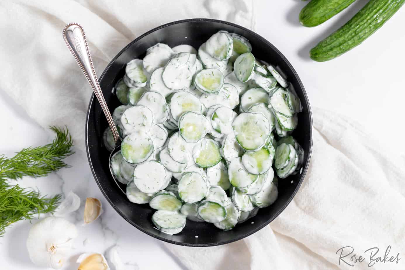 german cucumber salad tossed in a creamy white german dressing in a black bowl with a spoon