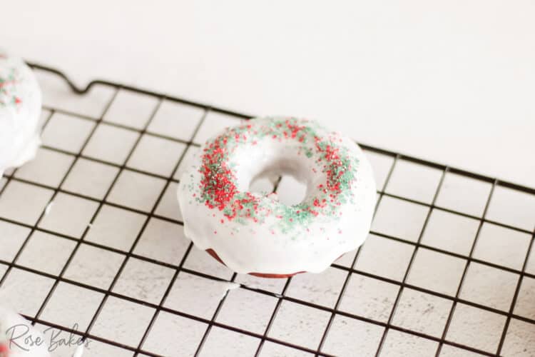 Red Velvet Donut that has been dipped in frosting and has red and green sugar sprinkles on a cooling rack