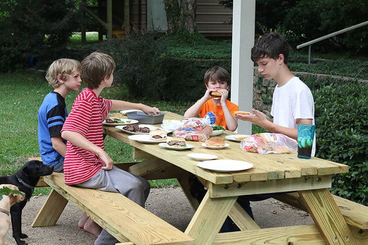 Kids at picnic table in back yard eating burgers