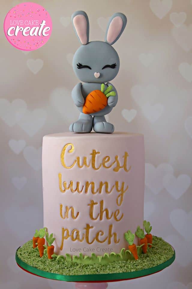 Gray Bunny Topper holding a carrot and Carrot Patch on cake board. The cake reads "Cutest bunny in the patch" on the front of the cake.