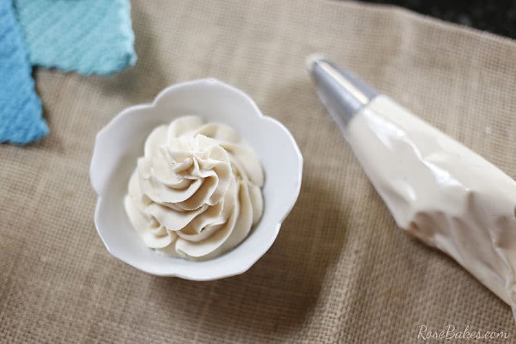 White bowl with a piped swirl of maple brown sugar buttercream. Next to it is a piping bag filled with the buttercream.