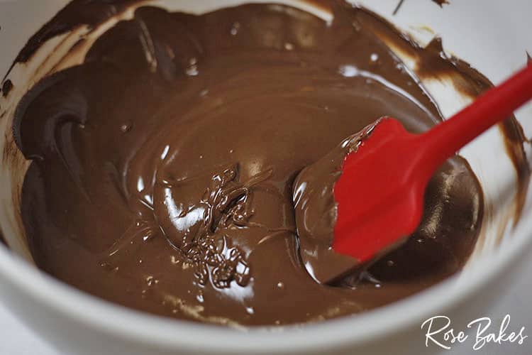 Melted chocolate in white bowl with red silicone spatula