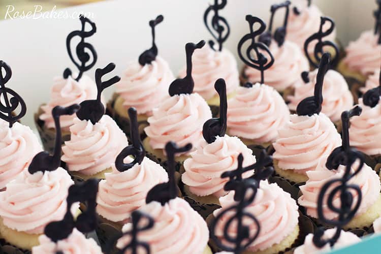 Cupcakes with light pink frosting and chocolate music note toppers.