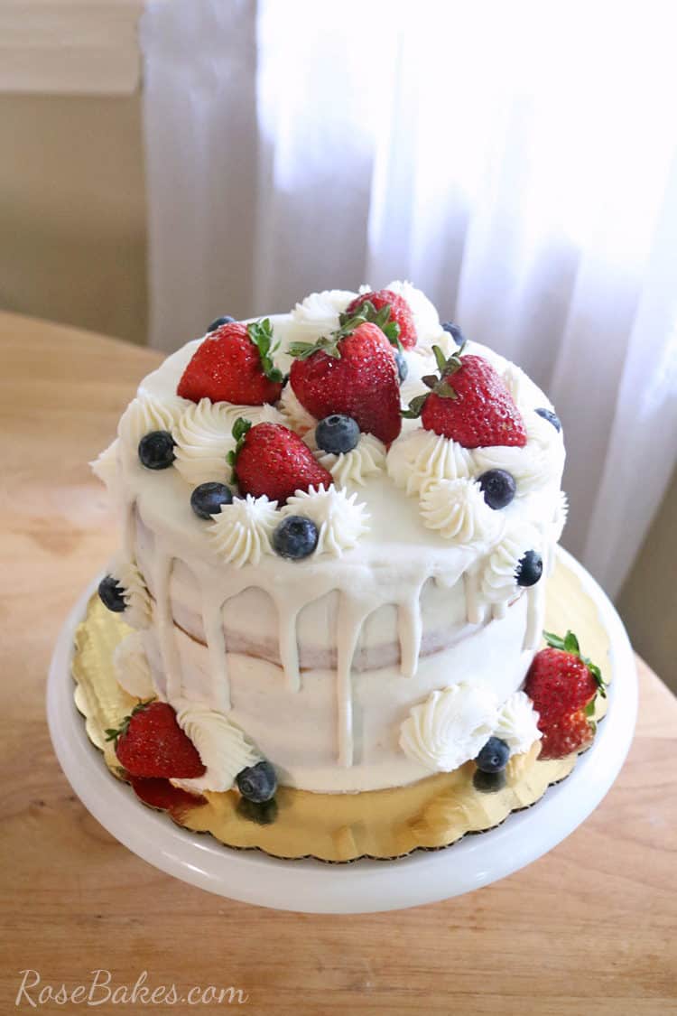 nearly naked cake with fresh fruit and white chocoate drip on a cake stand