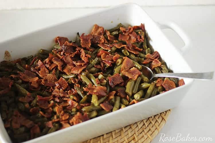 Green beans with crispy bacon in a white casserole dish and a serving spoon.