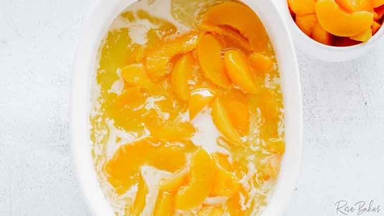 canned peaches in the batter and butter in a white oval casserole dish