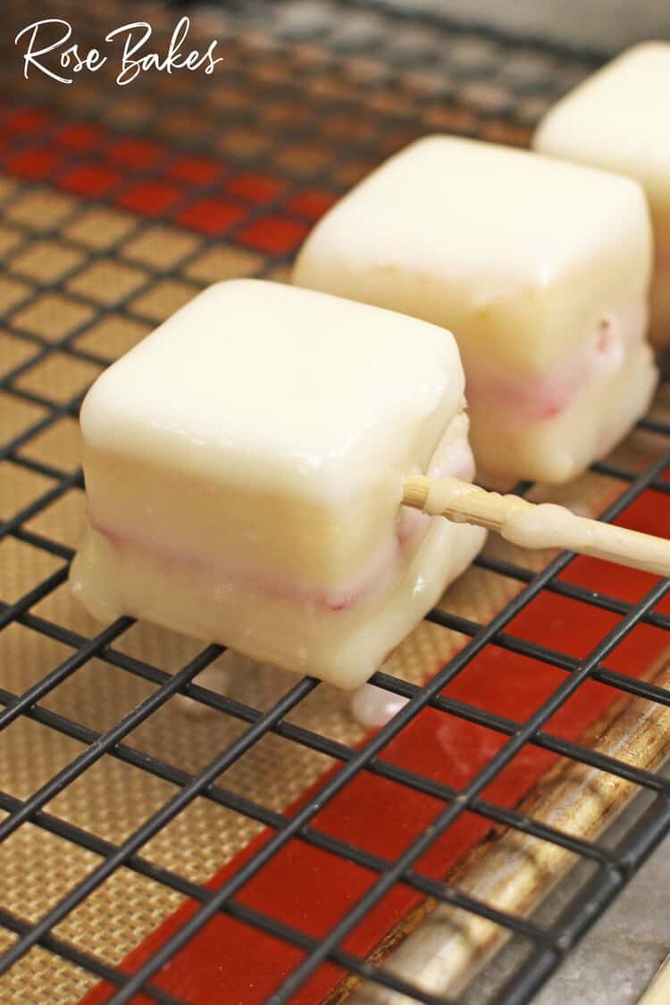 dipped petit four on a wire rack with the skewer being pulled out.