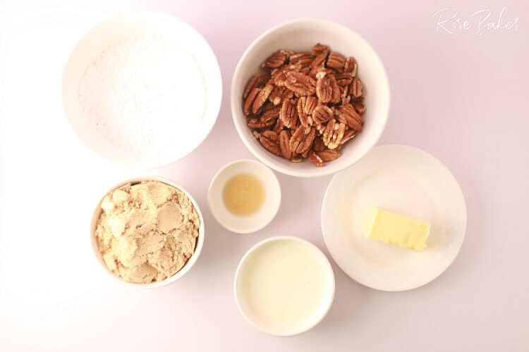 Ingredients for Pralines including pecans in bowl, brown sugar in bowl, vanilla in bowl, powdered sugar in bowl, heavy cream in bowl and butter on small plate