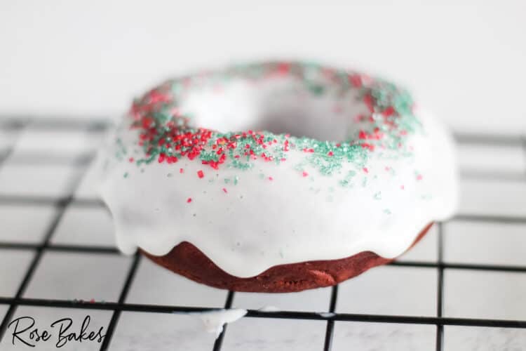 Red Velvet Donut that has been dipped in frosting and has red and green sugar sprinkles on a cooling rack