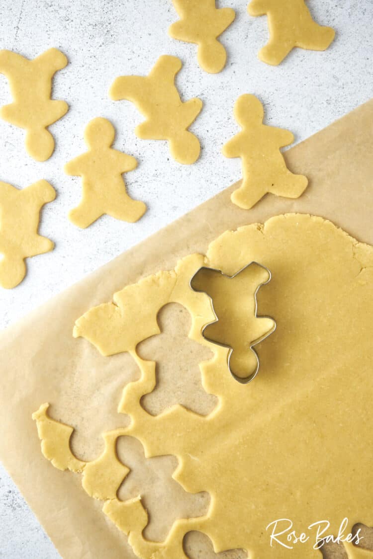 Sheet of cookie dough with shapes cut out with the gingerbread man cookie cutter.  It is turned upside down to make the reindeer shape.