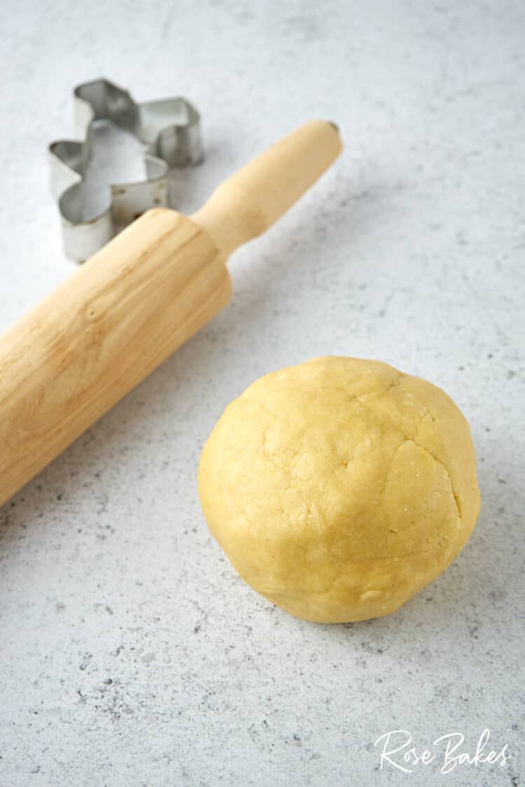 A softball sized ball of cookie dough, rolling pin, and cookie cutter