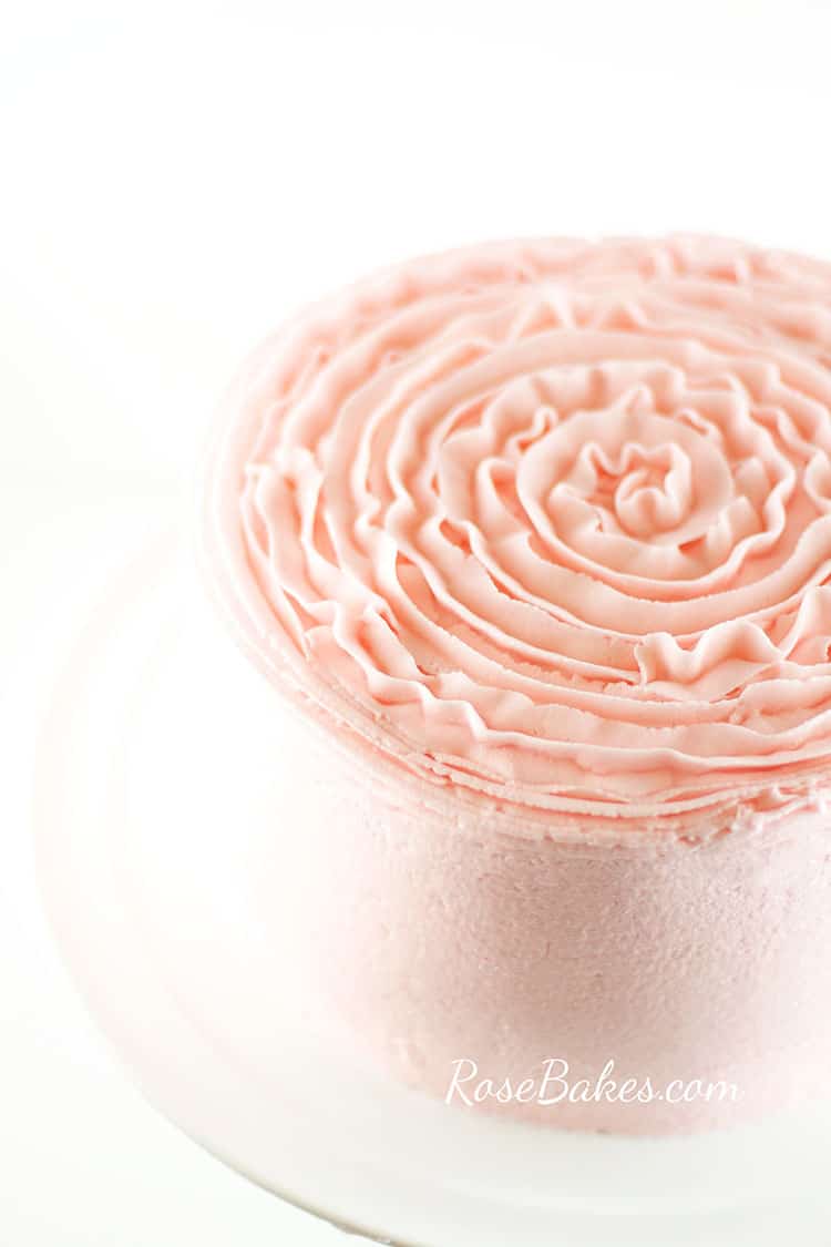 Cake frosted in light pink buttercream that is smooth on the sides and has a ruffly textured top.