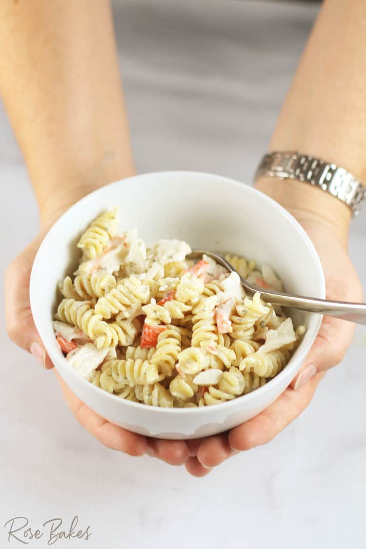 A bowl of Creamy Crab Pasta Salad in a white bowl with a fork being held by two hands 