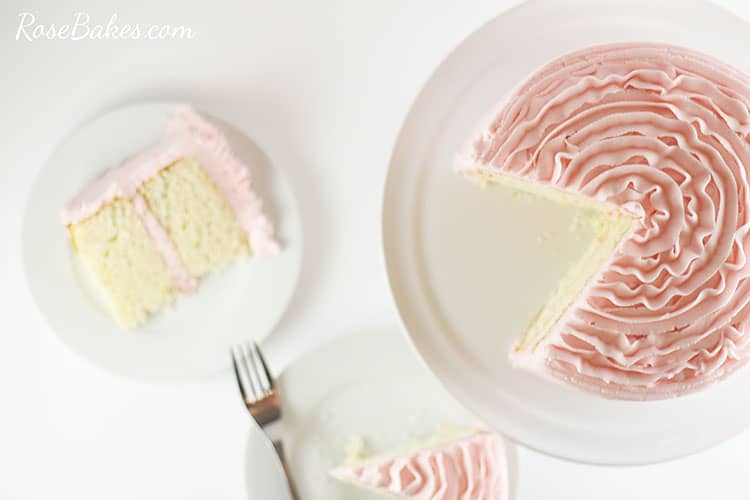 Overhead view of the light pink ruffle cake with a couple of slices taken out.  The slices of cake are beside the cake stand on white plates.