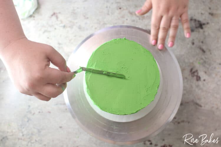 green buttercream icing being smoothed on cake tier with spatula not yet sharp edge 