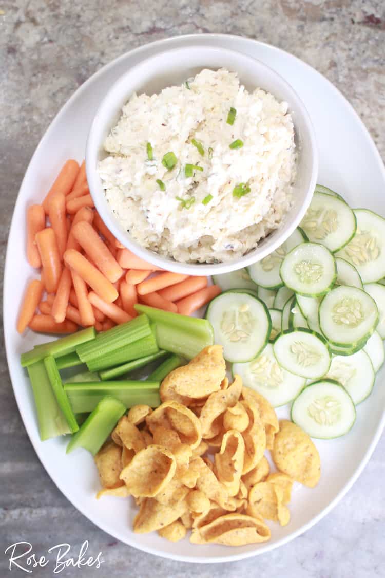 Large white platter filled with baby carrots, celery sticks, Frito Scoops, sliced cucumbers, and a bowl of the spicy cottage cheese dip.