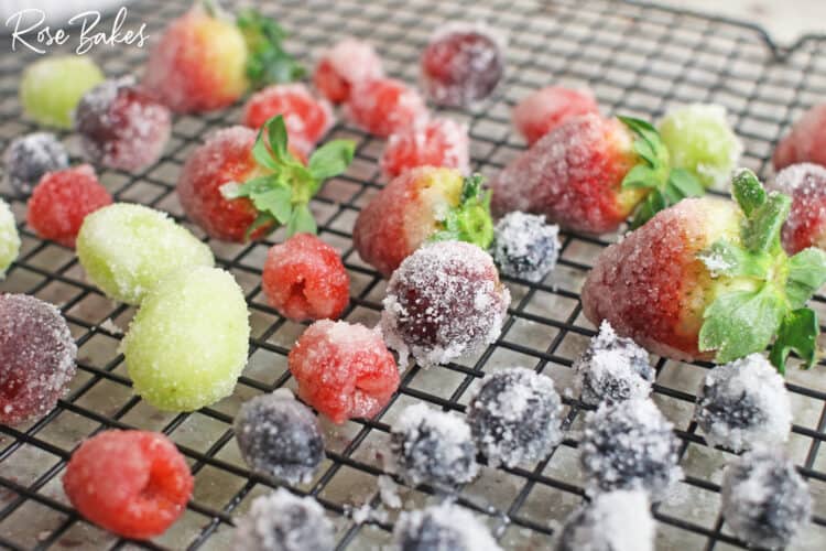 Grapes, blueberries, raspberries, and strawberries covered in sugar drying on a rack.