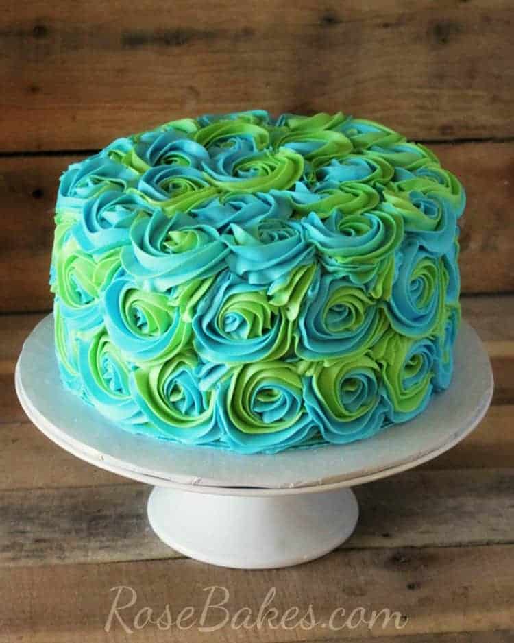 Turquoise & Lime Green Swirled Buttercream Roses Cake on a white cake stand with a wood backround