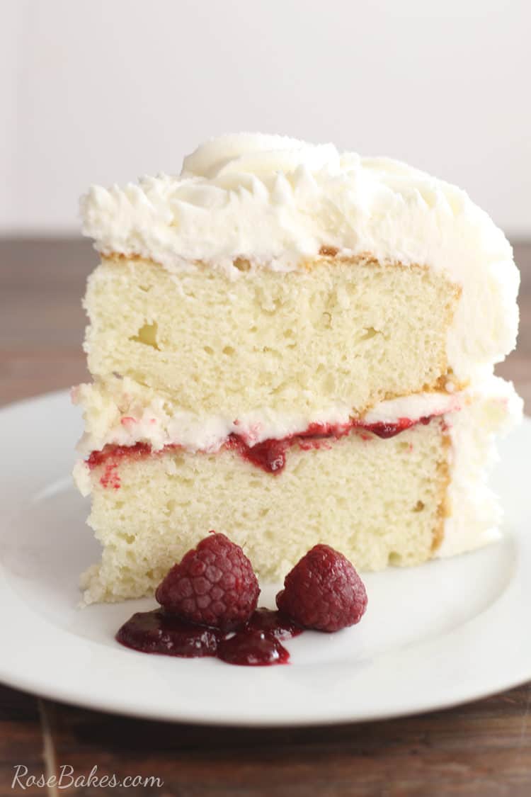 white cake with vanilla buttercream and raspberry filling on a white plate with fresh raspberries