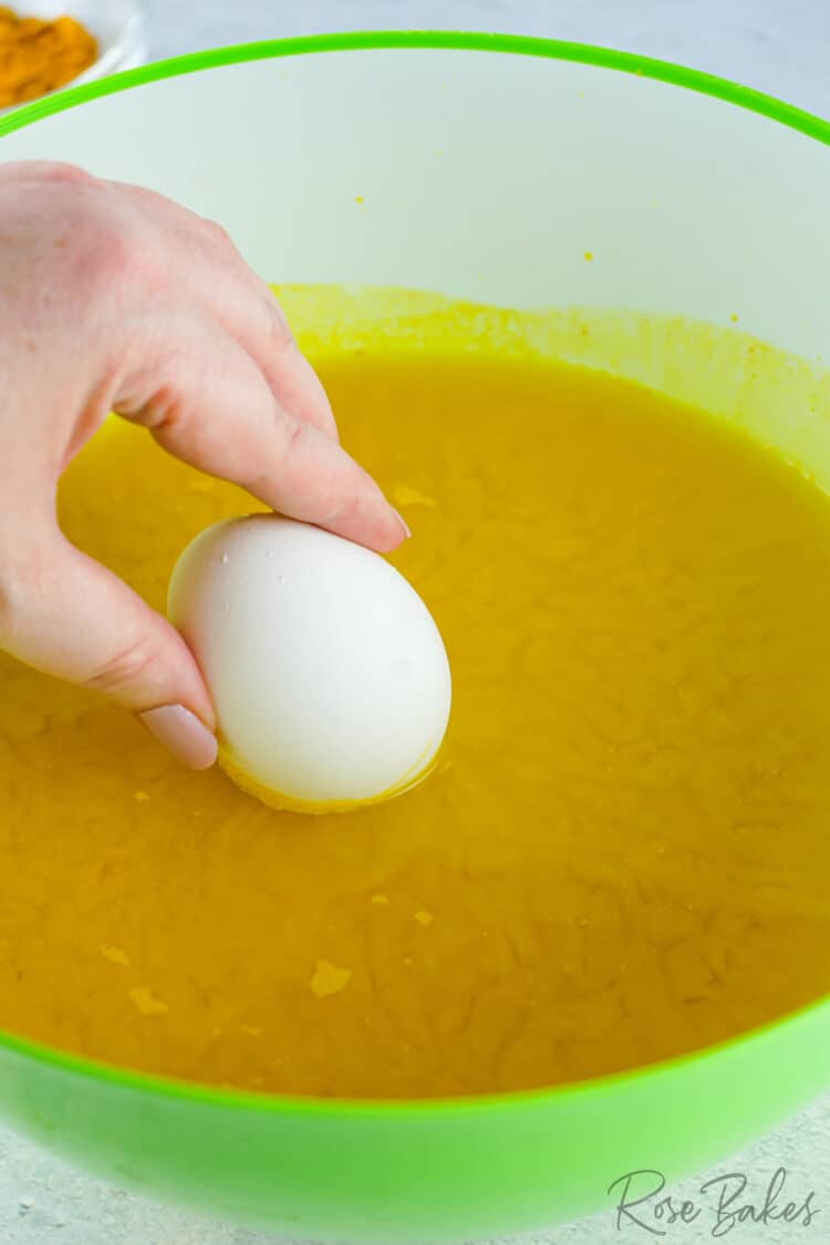 egg being dipped into water and turmeric mixture 