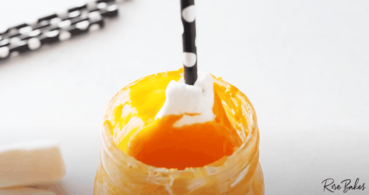 candy corn shaped marshmallow being dipped in orange colored candy melt