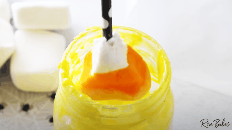candy corn shaped marshmallow being dipped in yellow colored candy melt